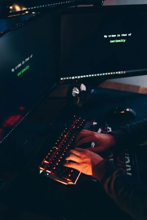 High angle of crop anonymous hacker stealing information from desktop computers with data on screens in twilight